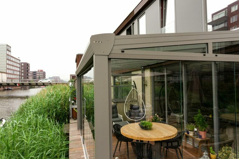 Kaltwintergarten am Wasser mit Sitzgruppe Terrassenüberdachung mit Glasschiebewänden am Wasser mit Sitzgruppe